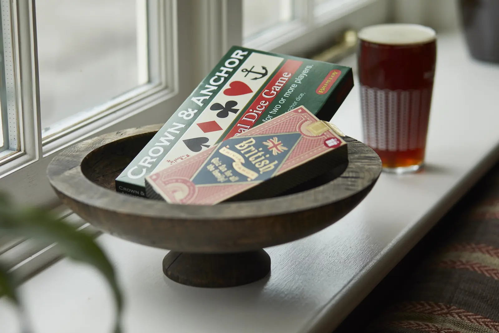 A Crown & Anchor dice game in a wooden bowl on the windowsill, beside a pint